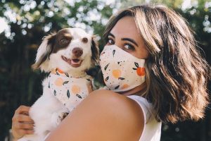 A girl is carrying a dog with matching bandana with her mask