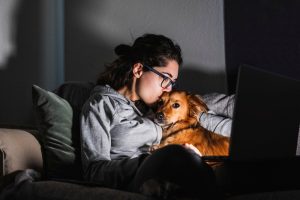 Dog mom kisses her dog while watching a movie on her computer at night.